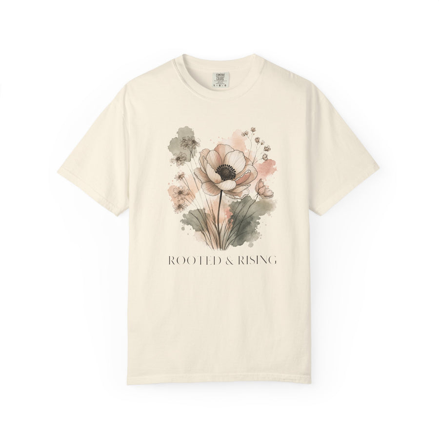 An off-white short-sleeve crewneck t-shirt featuring a watercolor floral graphic in soft pink, beige, and green tones, with the text 'ROOTED & RISING' printed below the flowers.
