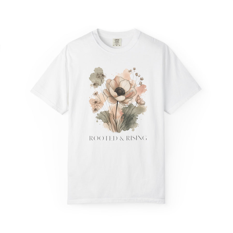 A white short-sleeve crewneck t-shirt featuring a watercolor floral graphic in soft pink, beige, and green tones, with the text 'ROOTED & RISING' printed below the flowers.
