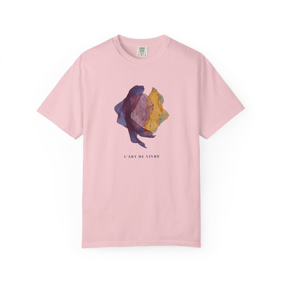 A light pink short-sleeve crewneck t-shirt featuring a central graphic of a stylized, abstract flower in purple, yellow, and blue tones, with the French text 'L'ART DE VIVRE' printed below it.